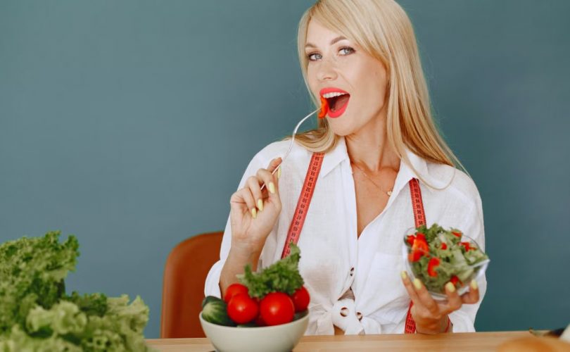 Woman enjoying a fresh salad with tomatoes and greens, promoting healthy eating.