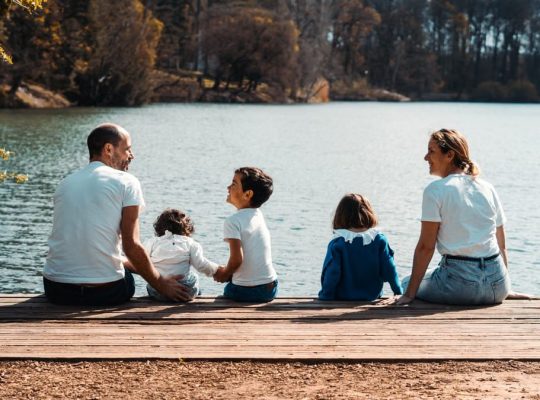 A family of five relaxing by a serene lake in Lyon, France on a sunny day.