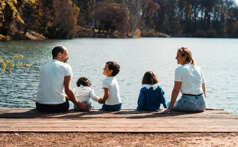 A family of five relaxing by a serene lake in Lyon, France on a sunny day.